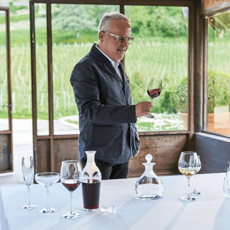 Man holding a clear stemmed wine glass at table with matching glassware