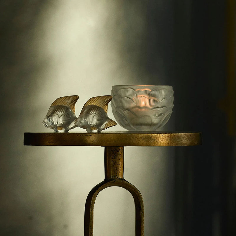 Gold-toned tray with two small fish sculptures and a clear glass votive cup