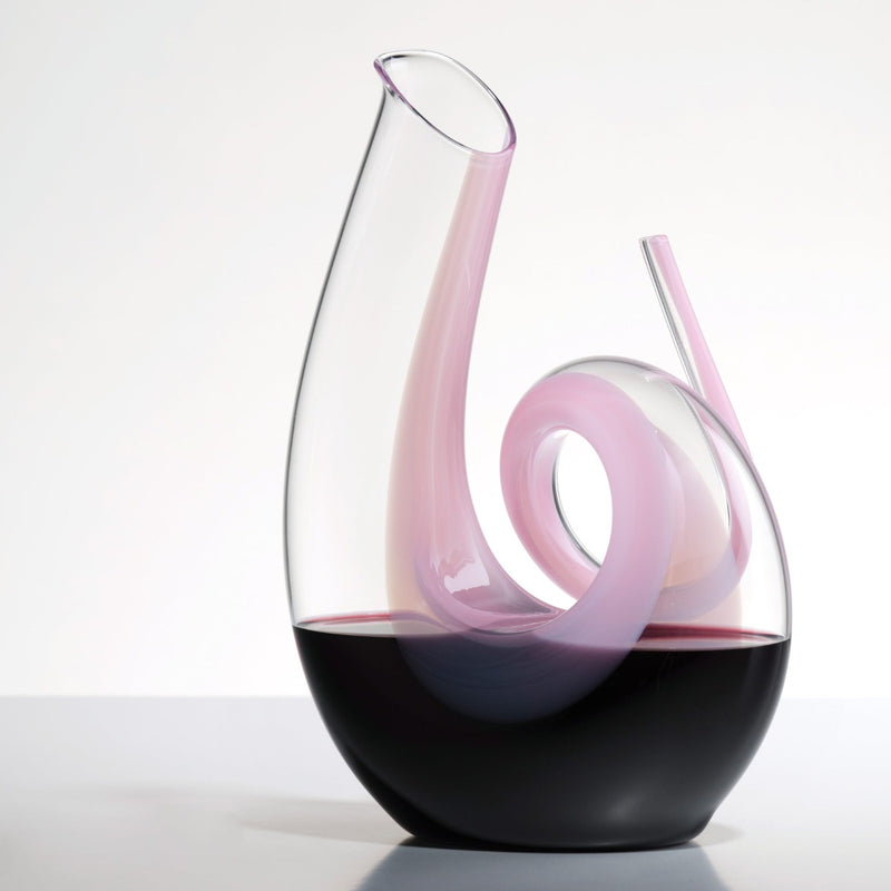 Riedel Crystal Pink Curly Decanter filled with red wine on a grey table